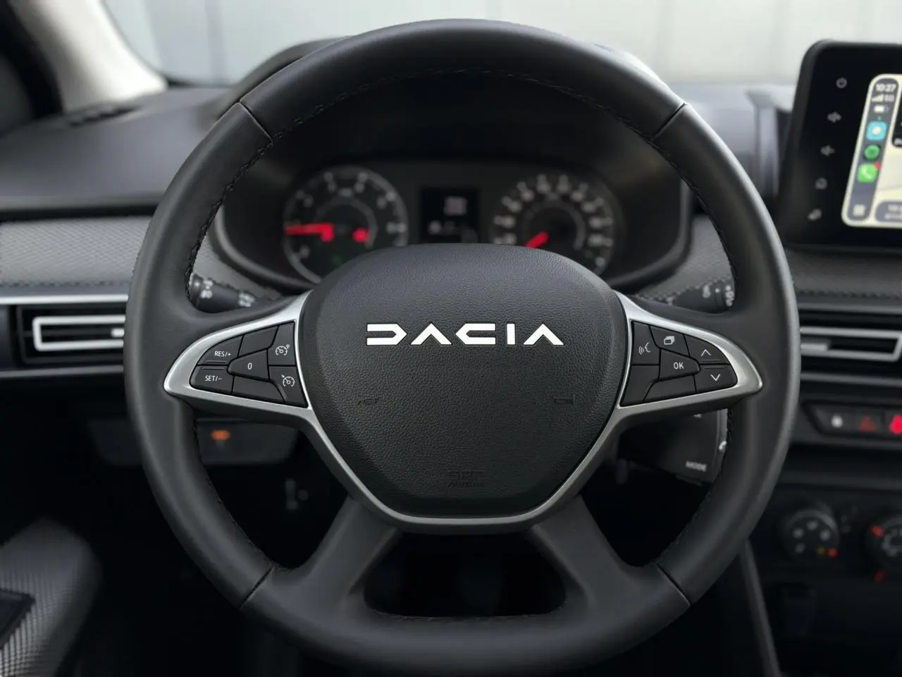 Vue rapprochée du volant noir de la Dacia Jogger 2024 avec commandes intégrées et tableau de bord en arrière-plan.