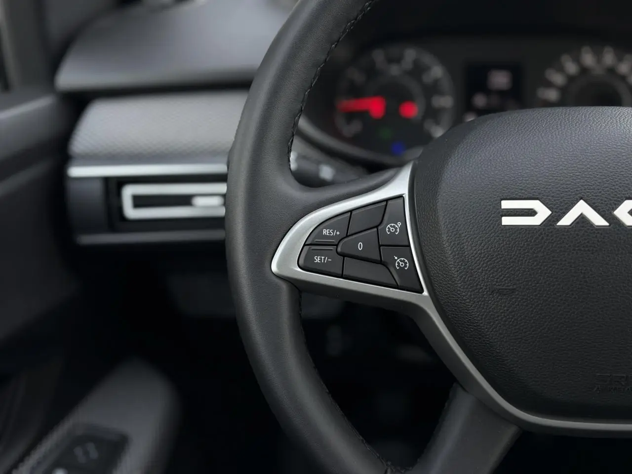 Gros plan sur le volant noir du Dacia Jogger 2024 avec commandes de régulateur de vitesse et tableau de bord flou.