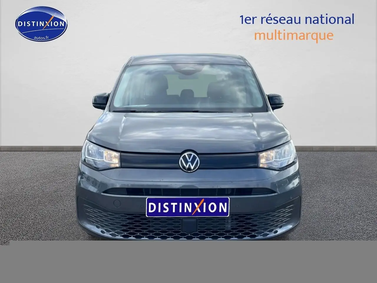 Vue frontale d'un Volkswagen Caddy gris indien 2025 avec calandre noire et phares allumés.