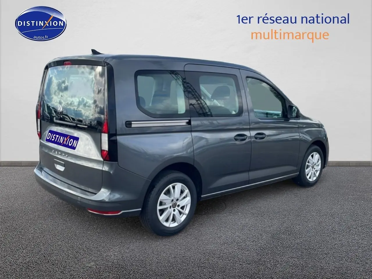 Vue 3/4 arrière droite d'un Volkswagen Caddy gris indien 2025 avec vitres teintées et barres de toit noires.