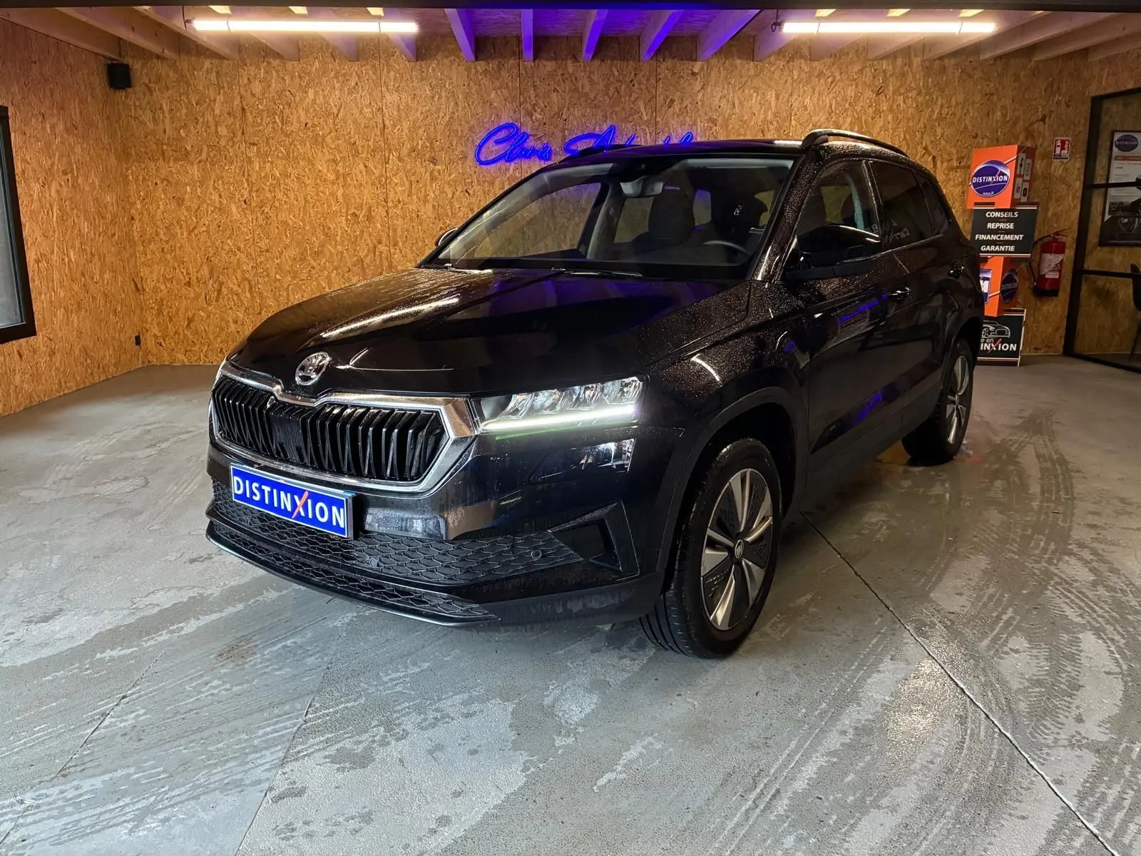 SKODA KAROQ noir 3/4 avant droit en intérieur, avec phares allumés et jantes alliage visibles.