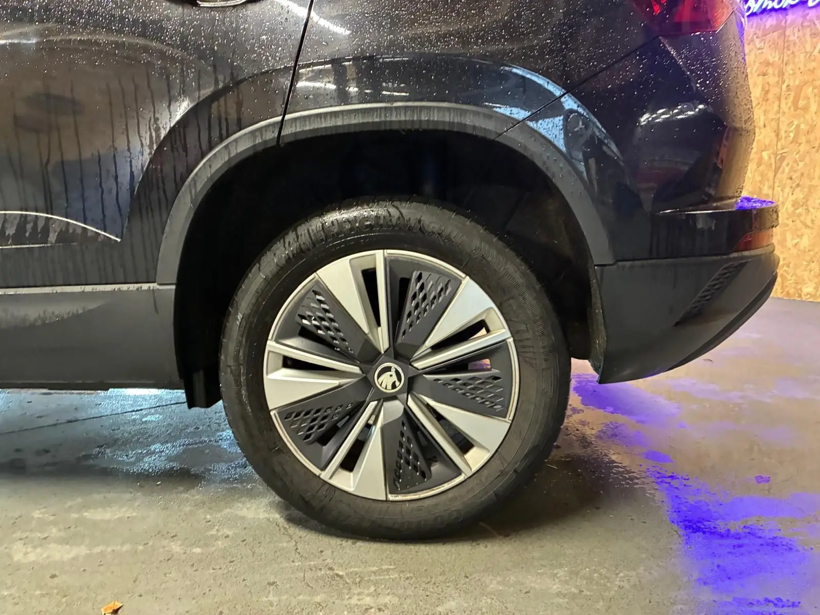 Vue latérale arrière droite du Skoda Karoq noir 2023, mettant en valeur la roue et la carrosserie mouillée.