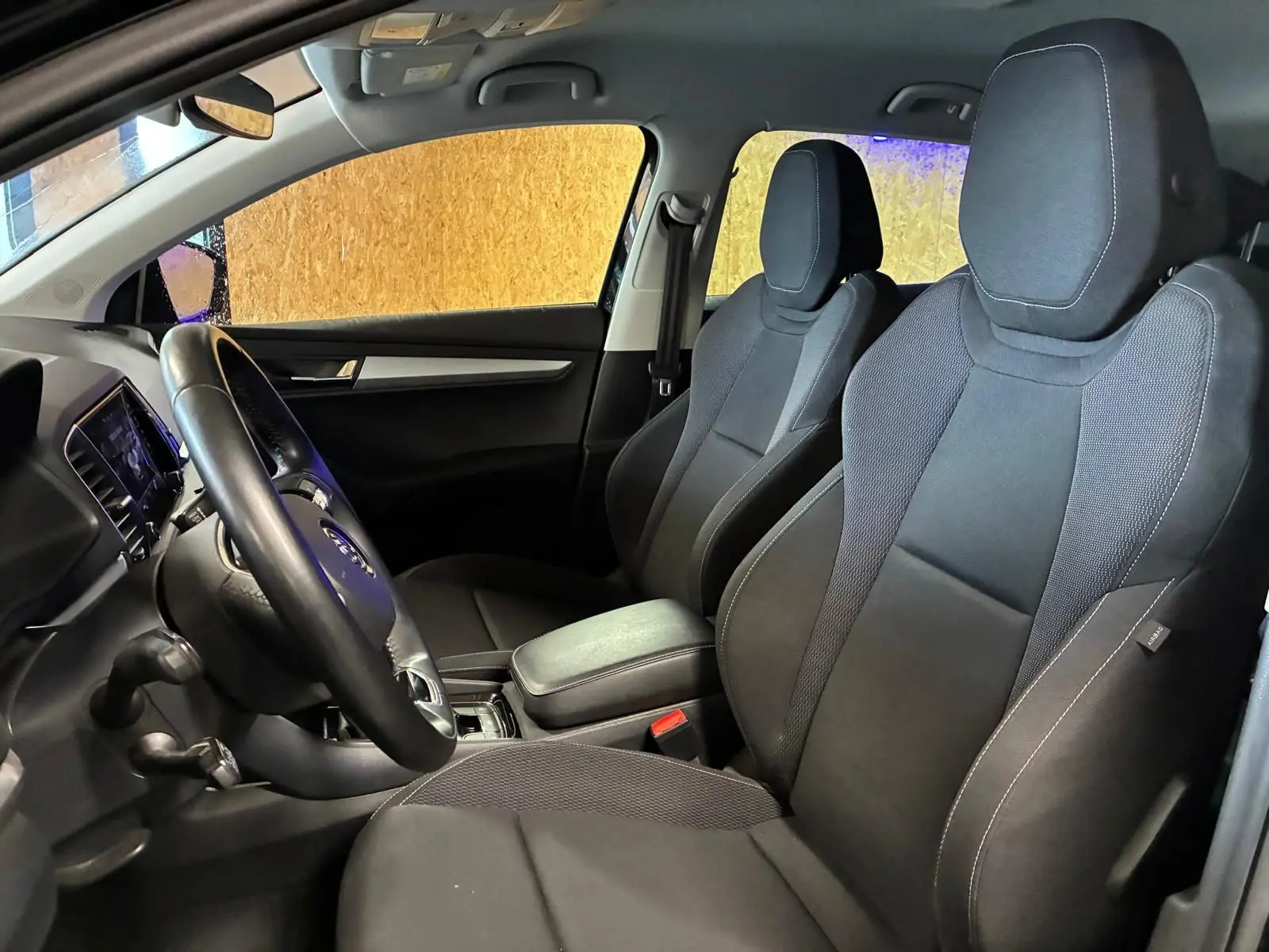 Vue intérieure côté conducteur du Skoda Karoq 2023, sièges tissu noir avec coutures contrastantes et tableau de bord moderne.