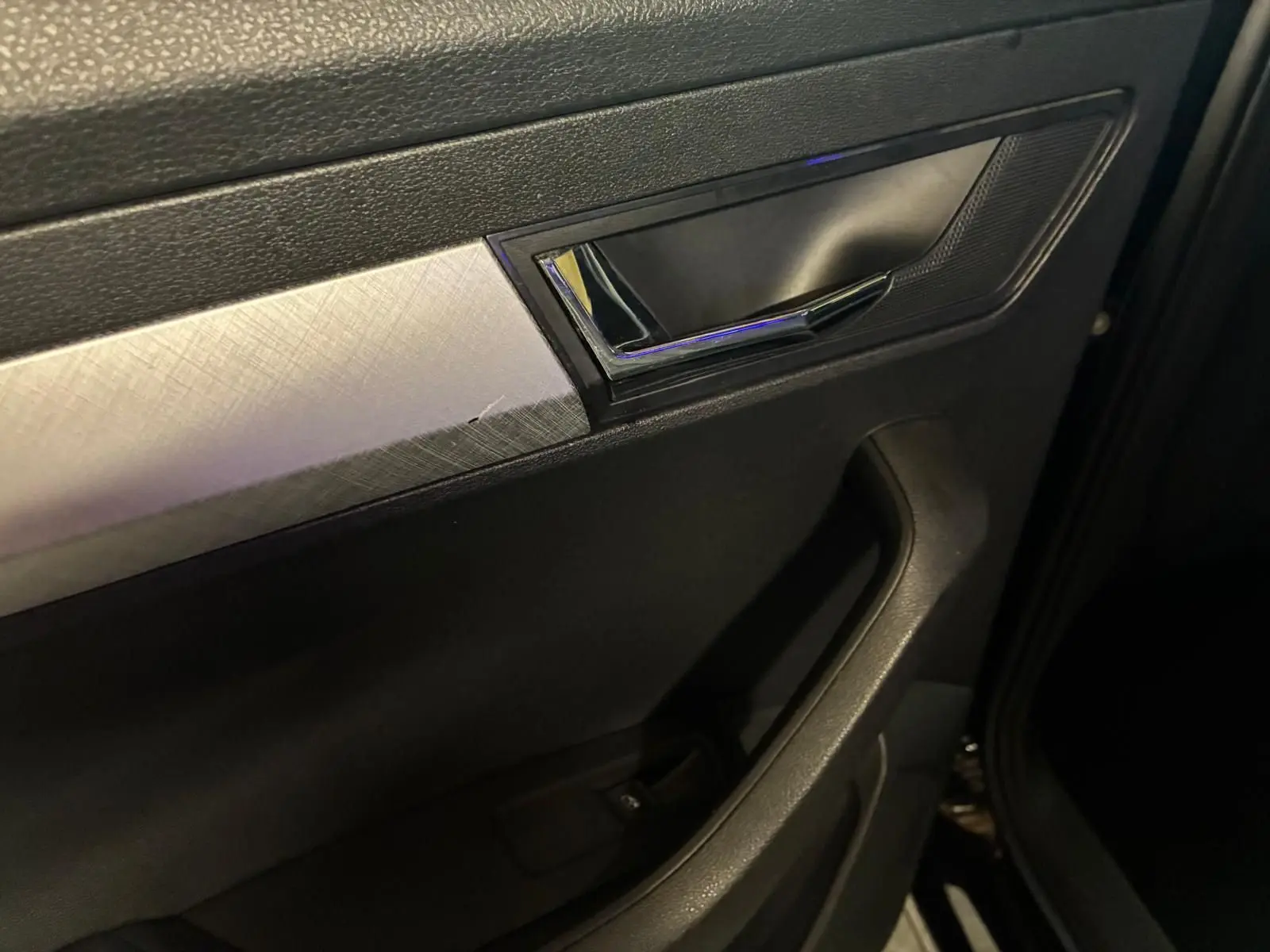 Détail de la poignée intérieure côté gauche d’une Skoda Karoq 2023 noire avec insert argenté texturé.