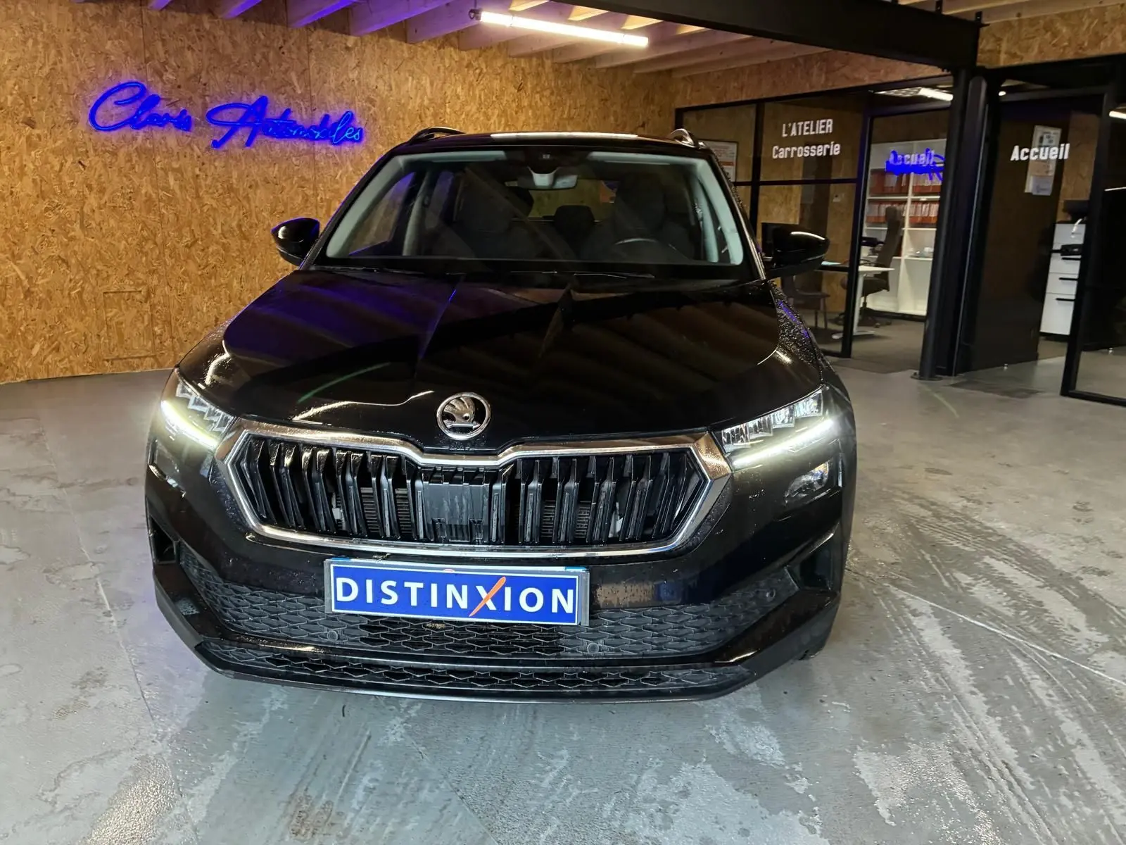Vue de face d’un Skoda Karoq noir 2023 avec phares allumés dans un showroom intérieur.