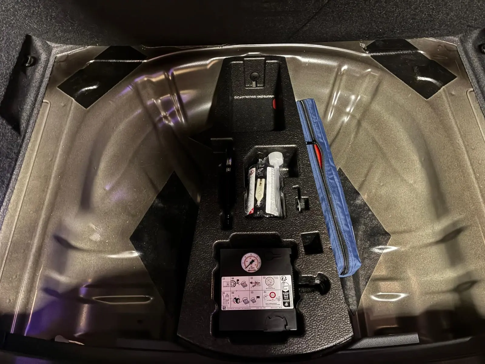 Vue plongeante sur le coffre ouvert d’un Skoda Karoq noir 2023, montrant le rangement sous plancher avec kit de réparation pneus.