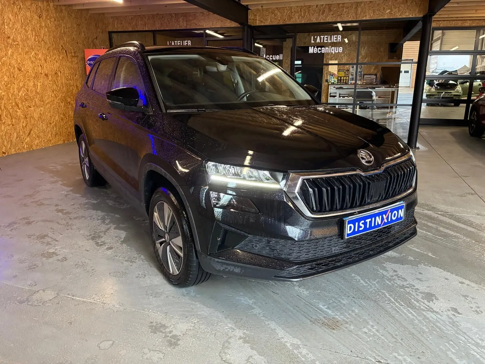 SKODA KAROQ noir 2023 vu en 3/4 avant droit dans un garage avec phares allumés et calandre distinctive.
