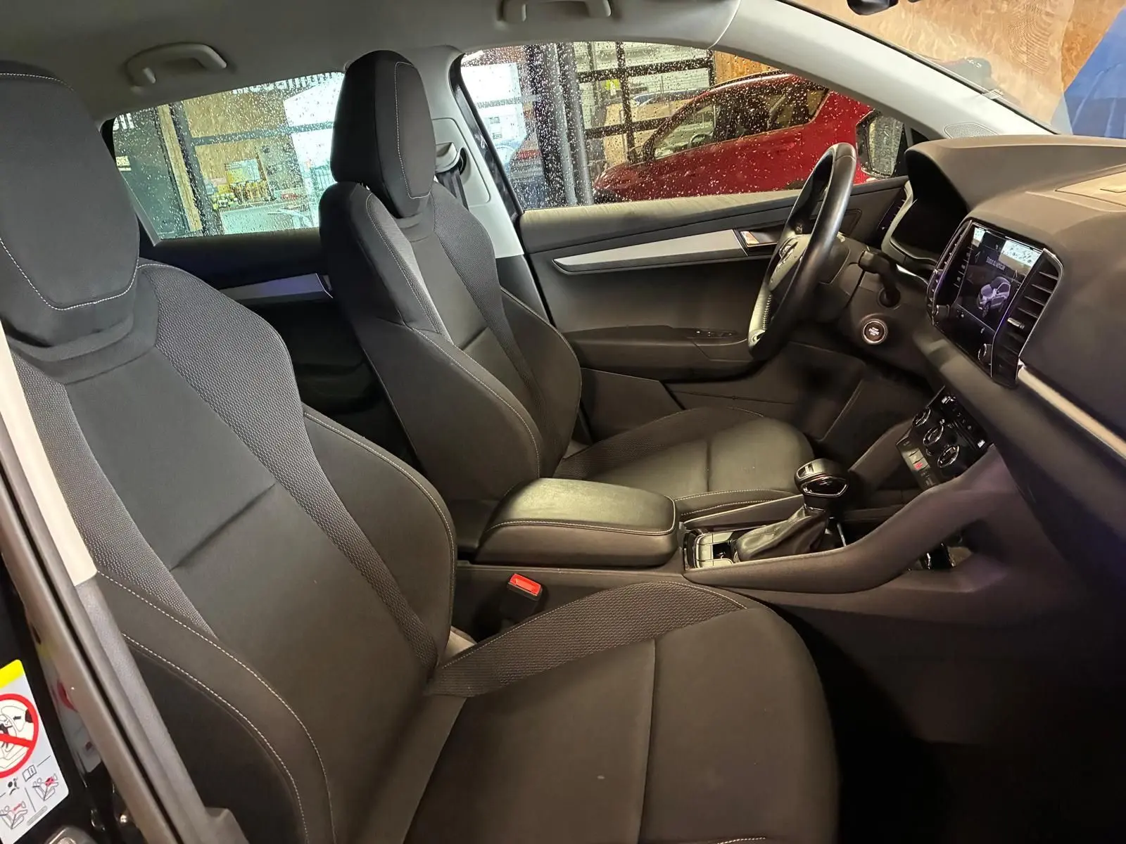 Vue intérieure côté conducteur du Skoda Karoq noir 2023, sièges tissu noir et tableau de bord avec écran tactile.