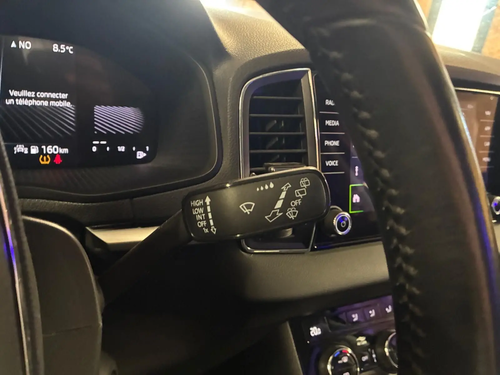 Vue intérieure rapprochée du volant et du commodo d’essuie-glace du Skoda Karoq noir 2023 avec tableau de bord digital.