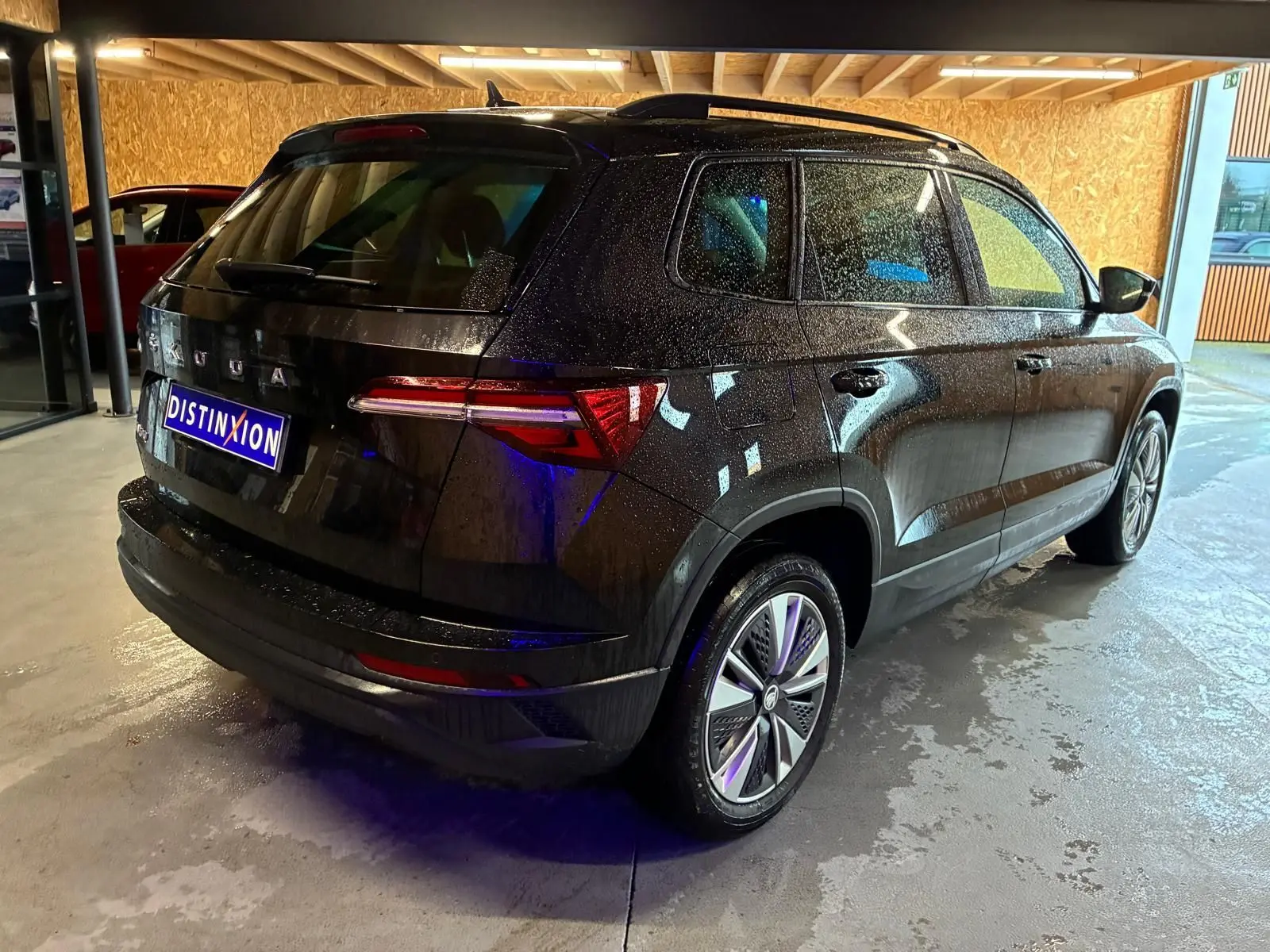 Vue 3/4 arrière droite d’un Skoda Karoq noir 2023 avec jantes alliage et feux arrière LED, stationné en intérieur.