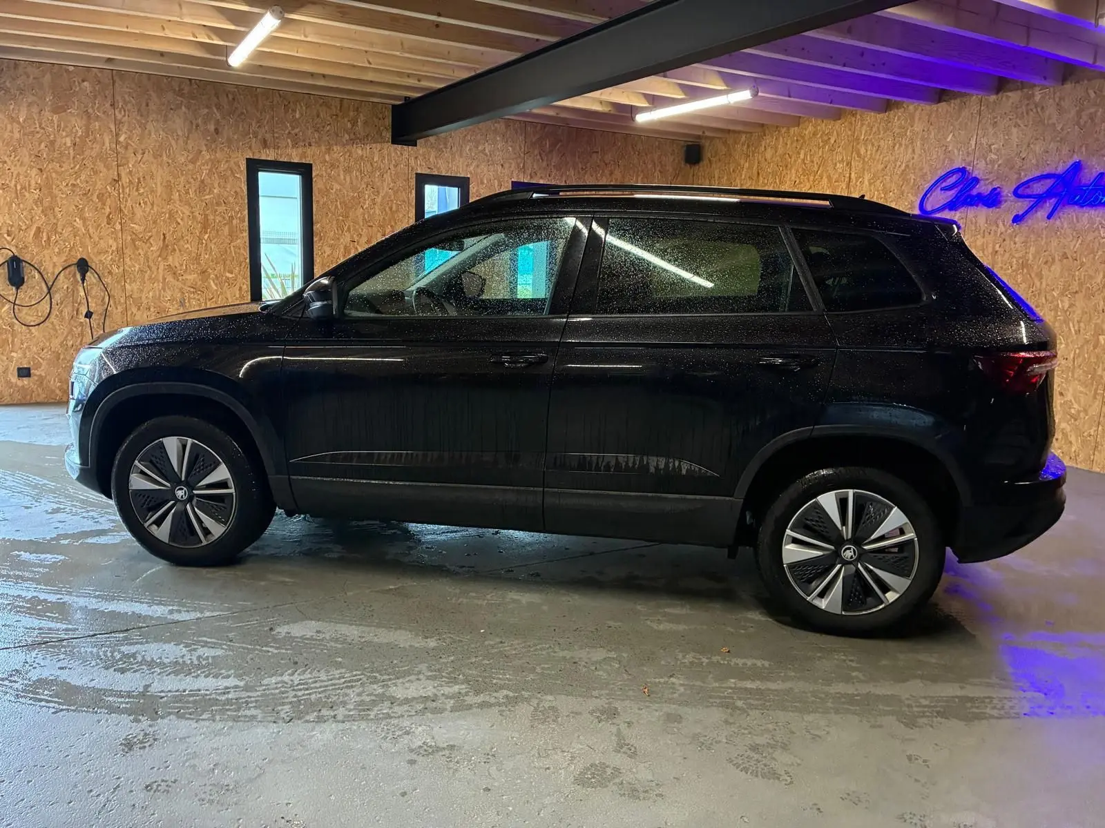 Vue de profil côté gauche d'un Skoda Karoq noir 2023 dans un garage avec murs en bois et sol béton humide.