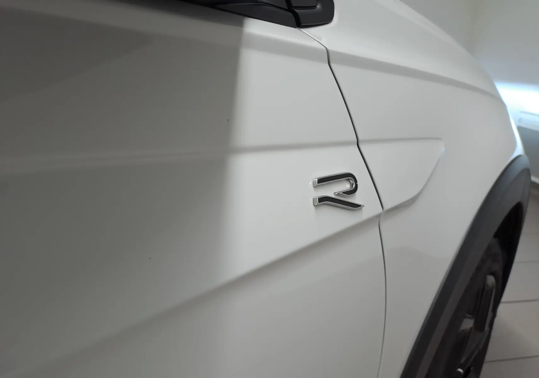 Gros plan sur l'aile avant droite blanche du Volkswagen Taigo avec logo R-Line brillant et jante noire partielle visible.