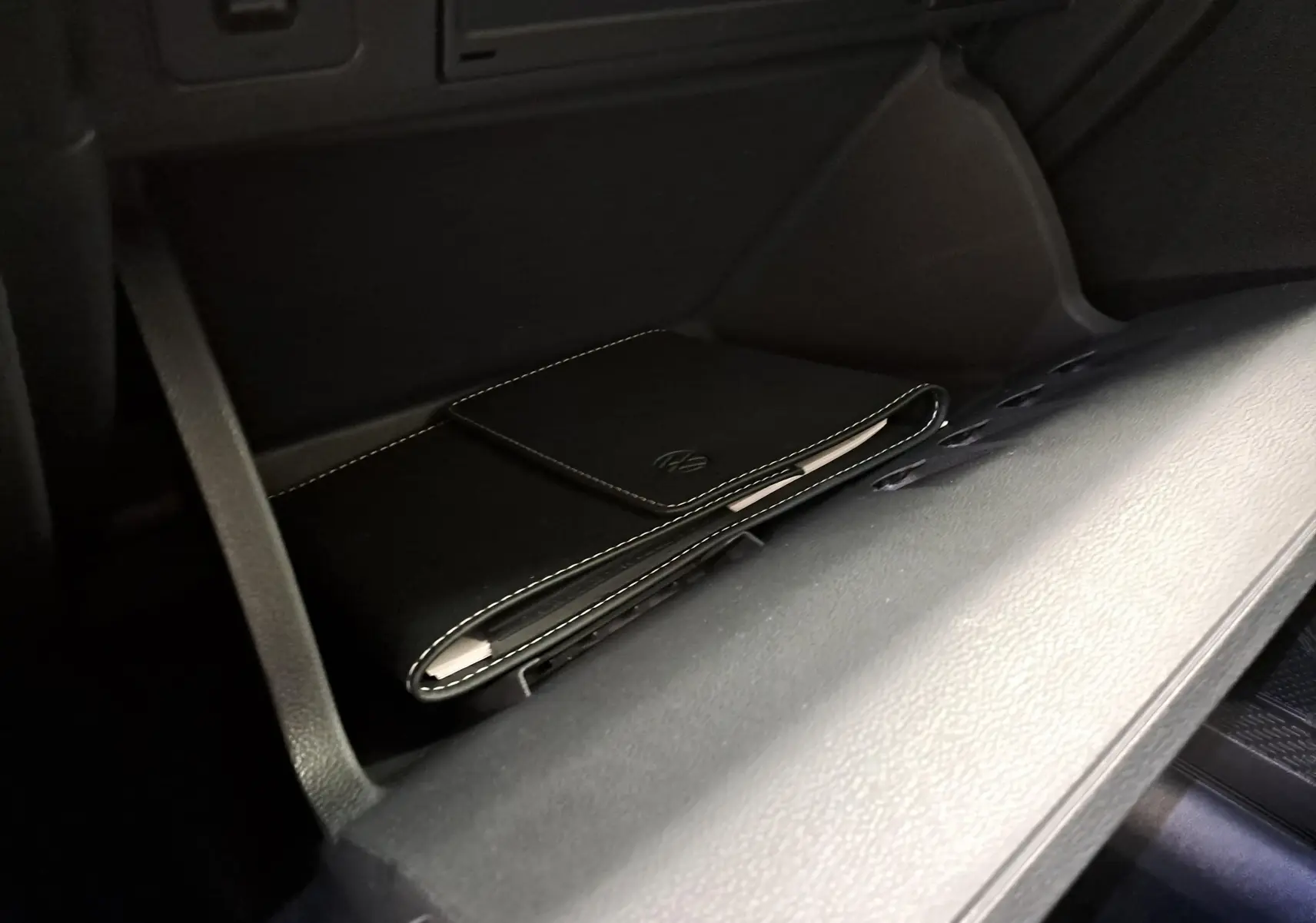 Détail de la boîte à gants ouverte avec pochette noire siglée Volkswagen dans un Volkswagen Taigo blanc toit noir.