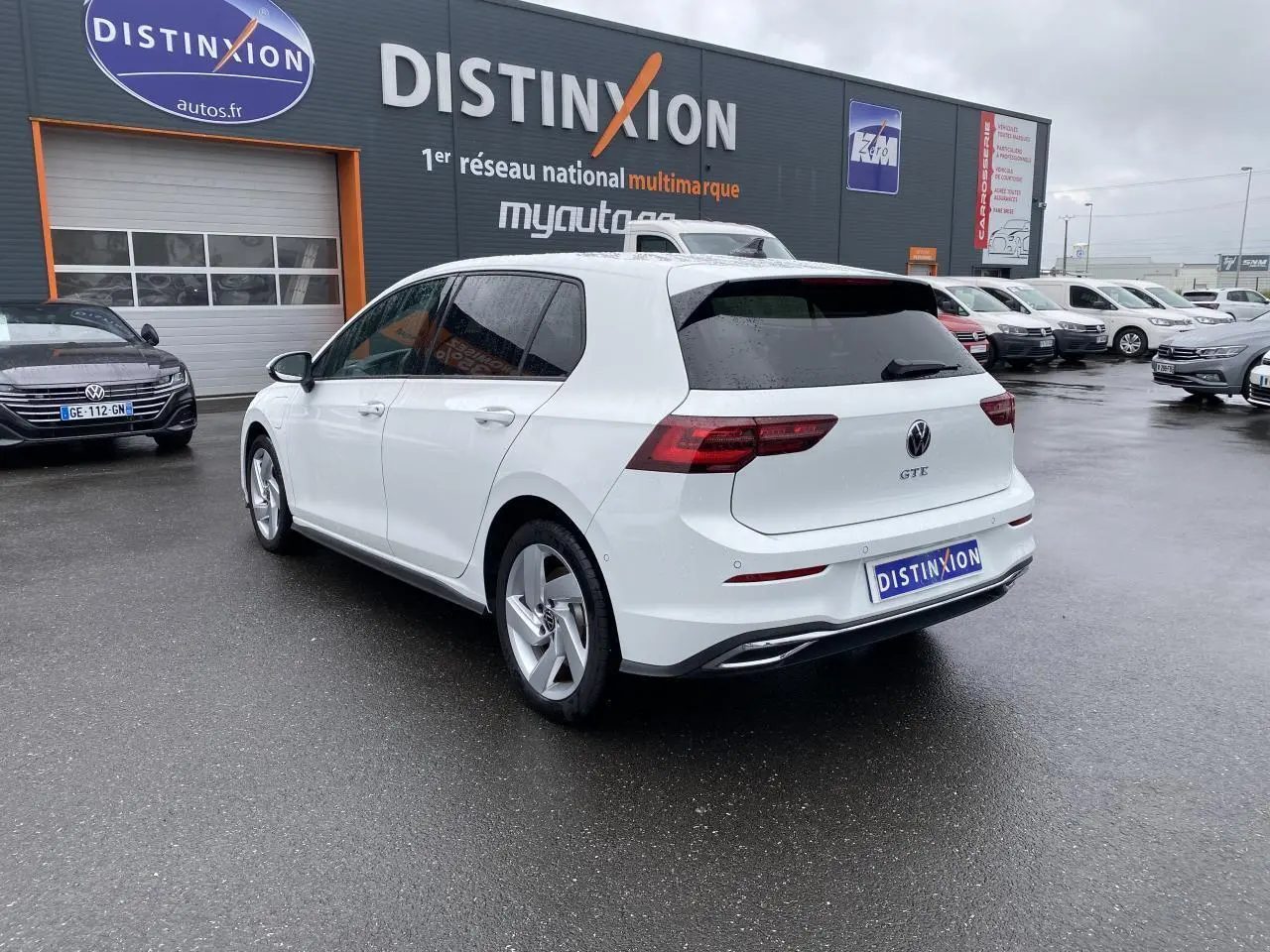 Vue 3/4 arrière droite d'une Volkswagen Golf VIII GTE blanche pur avec vitres surteintées sur parking humide.