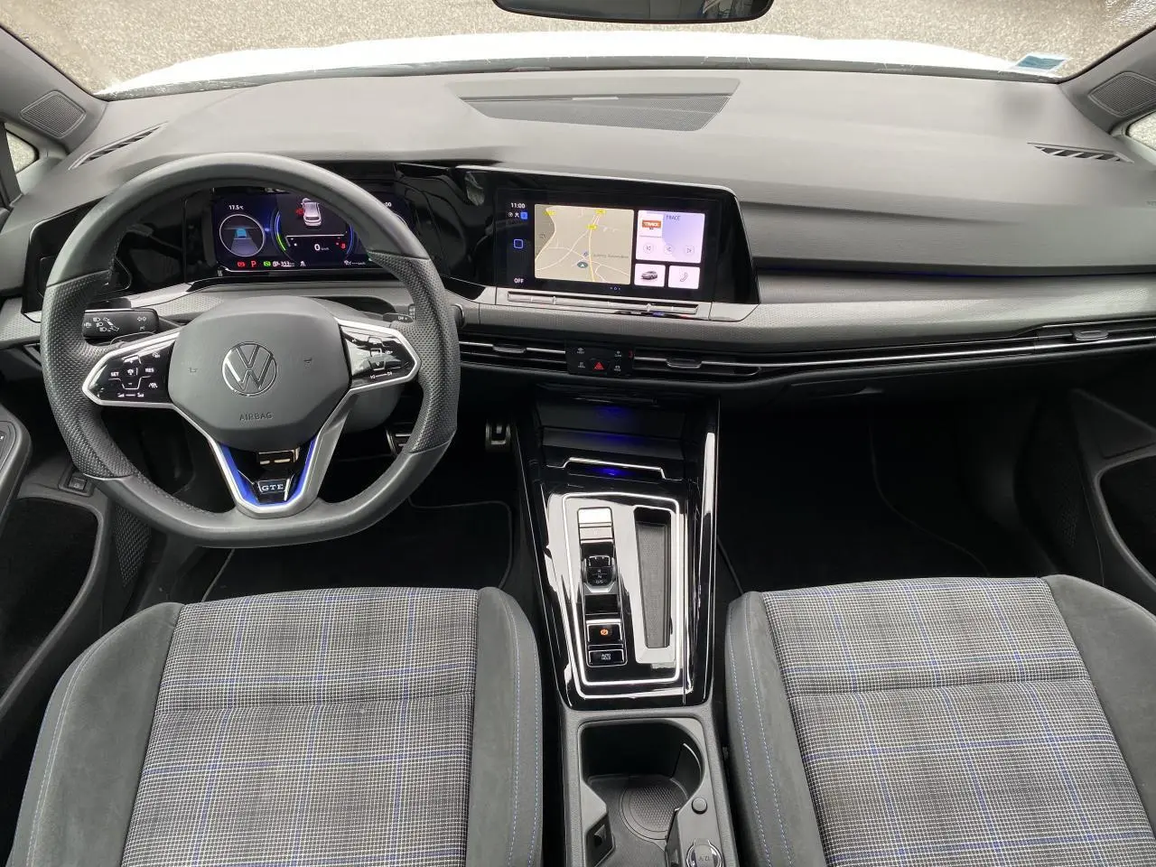 Vue intérieure avant de la Volkswagen Golf 1.4 eHybrid 2023, volant sport GTE et écran tactile central lumineux.
