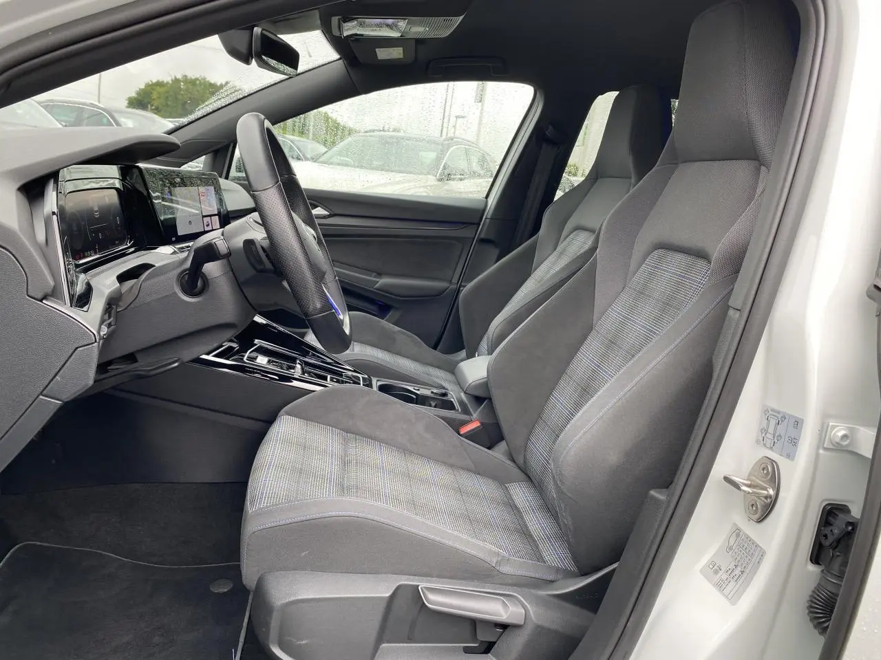 Intérieur côté conducteur de la Volkswagen Golf 1.4 eHybrid 2023, sièges tissu gris à motifs et volant sport cuir GTE.