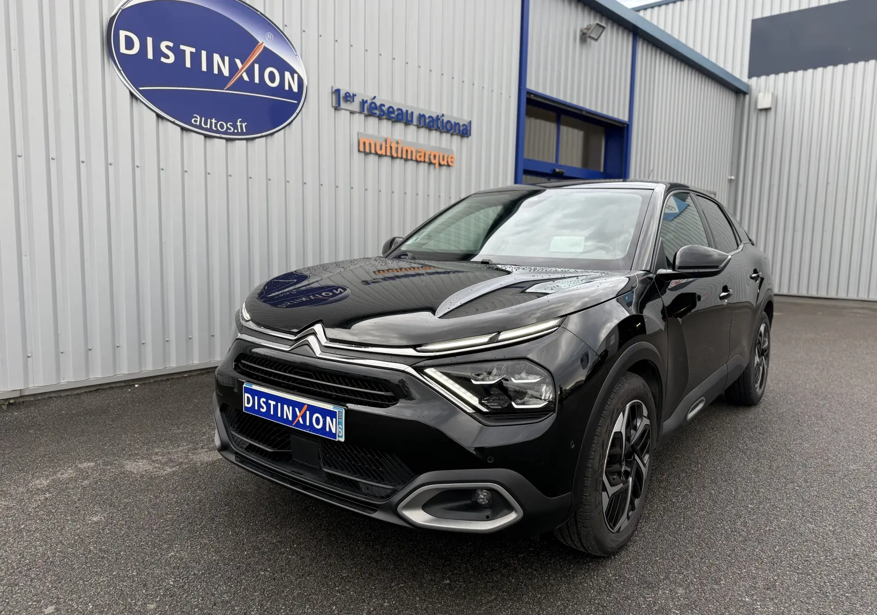 Citroën C4 noire vue 3/4 avant droit, avec calandre distinctive et phares LED modernes, stationnée devant un bâtiment.