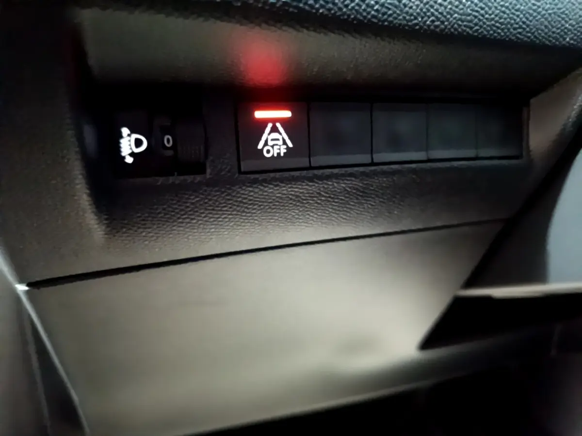 Gros plan sur les commandes noires du tableau de bord côté gauche du Peugeot 208 blanc, voyant d'alerte allumé rouge.