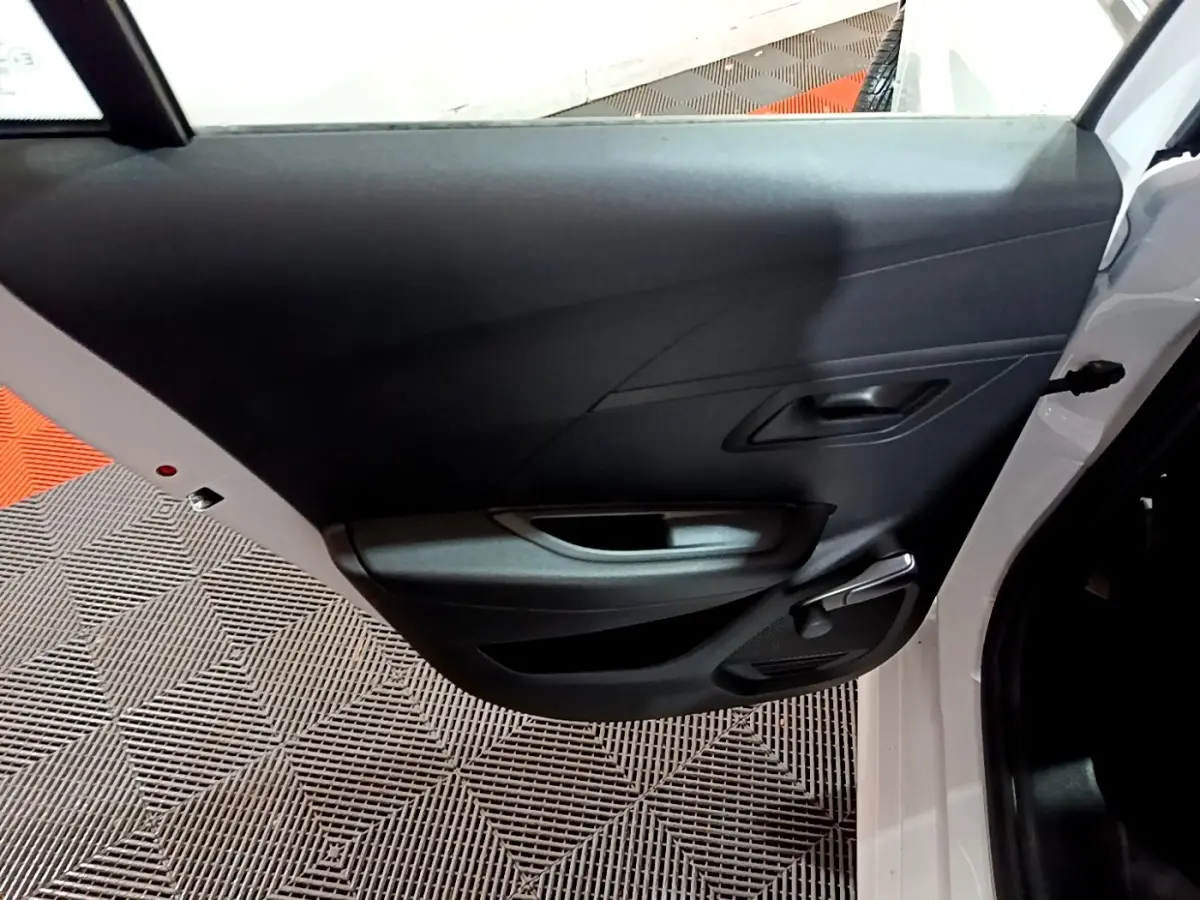 Vue intérieure de la porte arrière droite blanche d'une Peugeot 208 1.5 BlueHDi 100 S&S Premium avec poignée et manivelle de vitre.