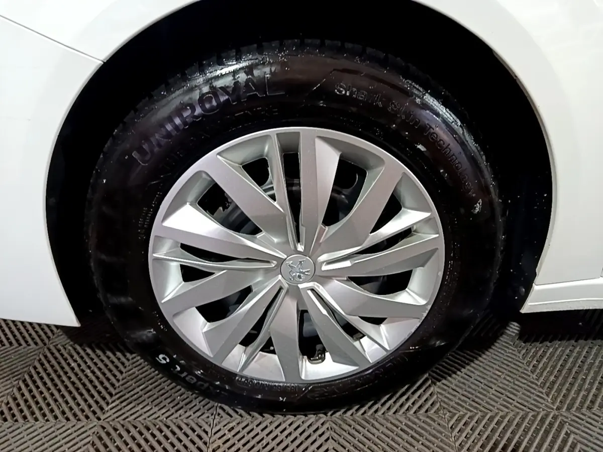 Gros plan sur la roue avant droite d'une Peugeot 208 blanche, mettant en valeur la jante argentée au design moderne.