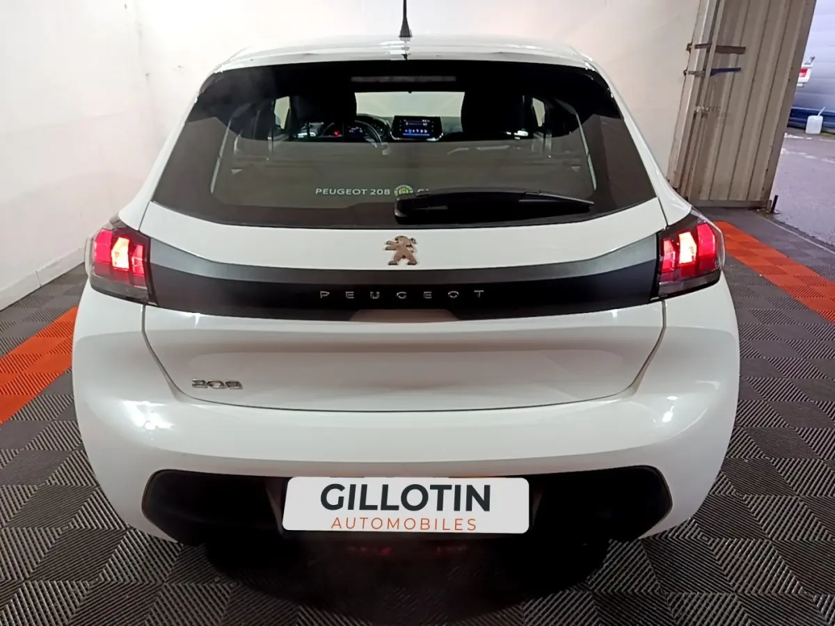 Vue arrière d'une Peugeot 208 blanche de 2021 avec feux LED allumés et logo lion central sur bande noire.