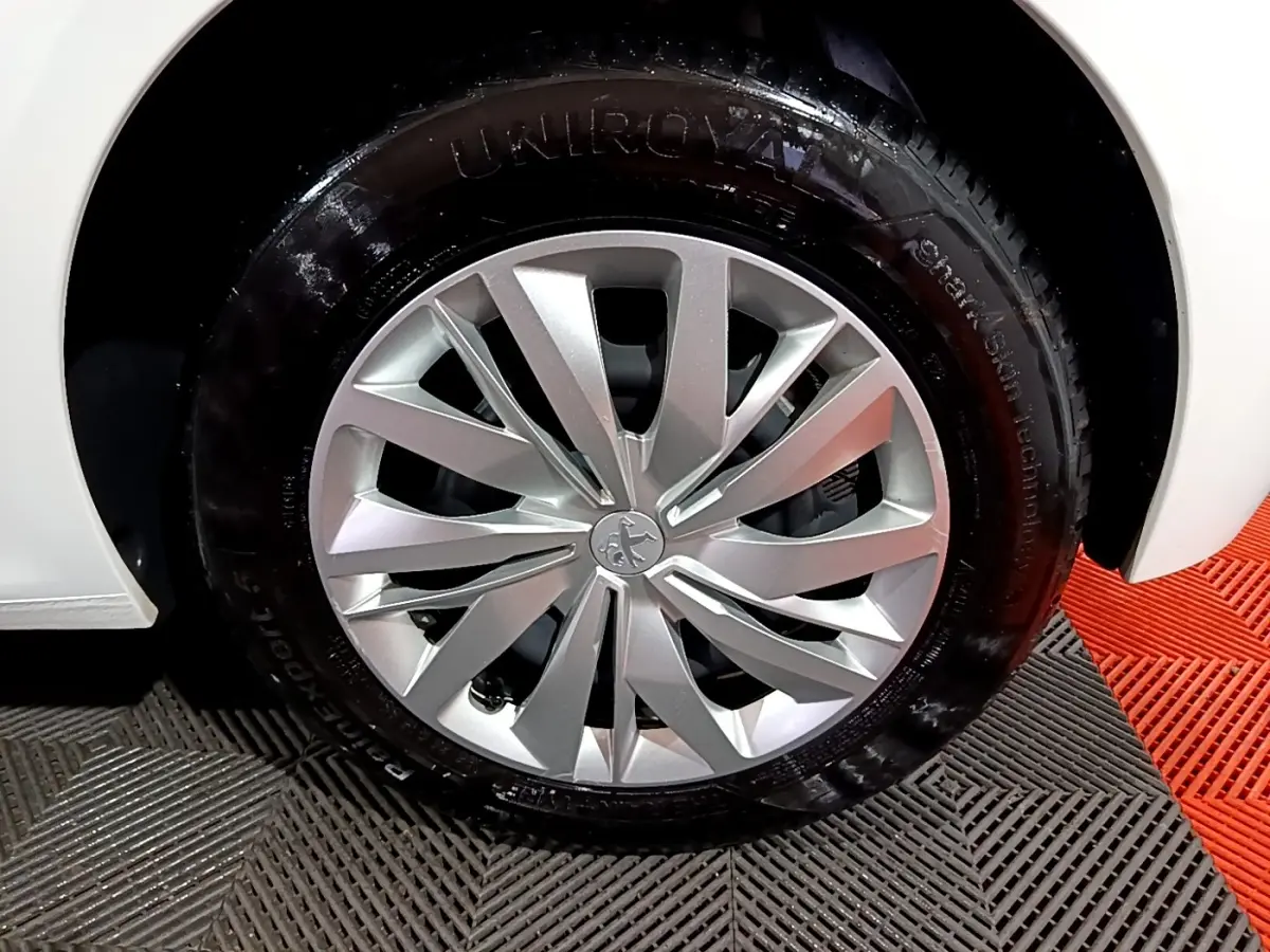 Gros plan sur la roue avant droite d'une Peugeot 208 blanche, mettant en valeur la jante argentée au design moderne.