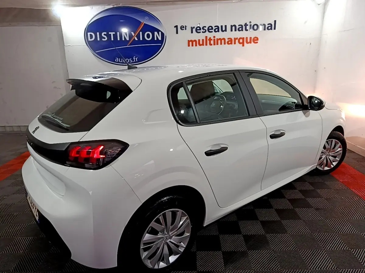 Vue 3/4 arrière droite d'une Peugeot 208 blanche avec feux arrière LED et jantes alliage dans un showroom.