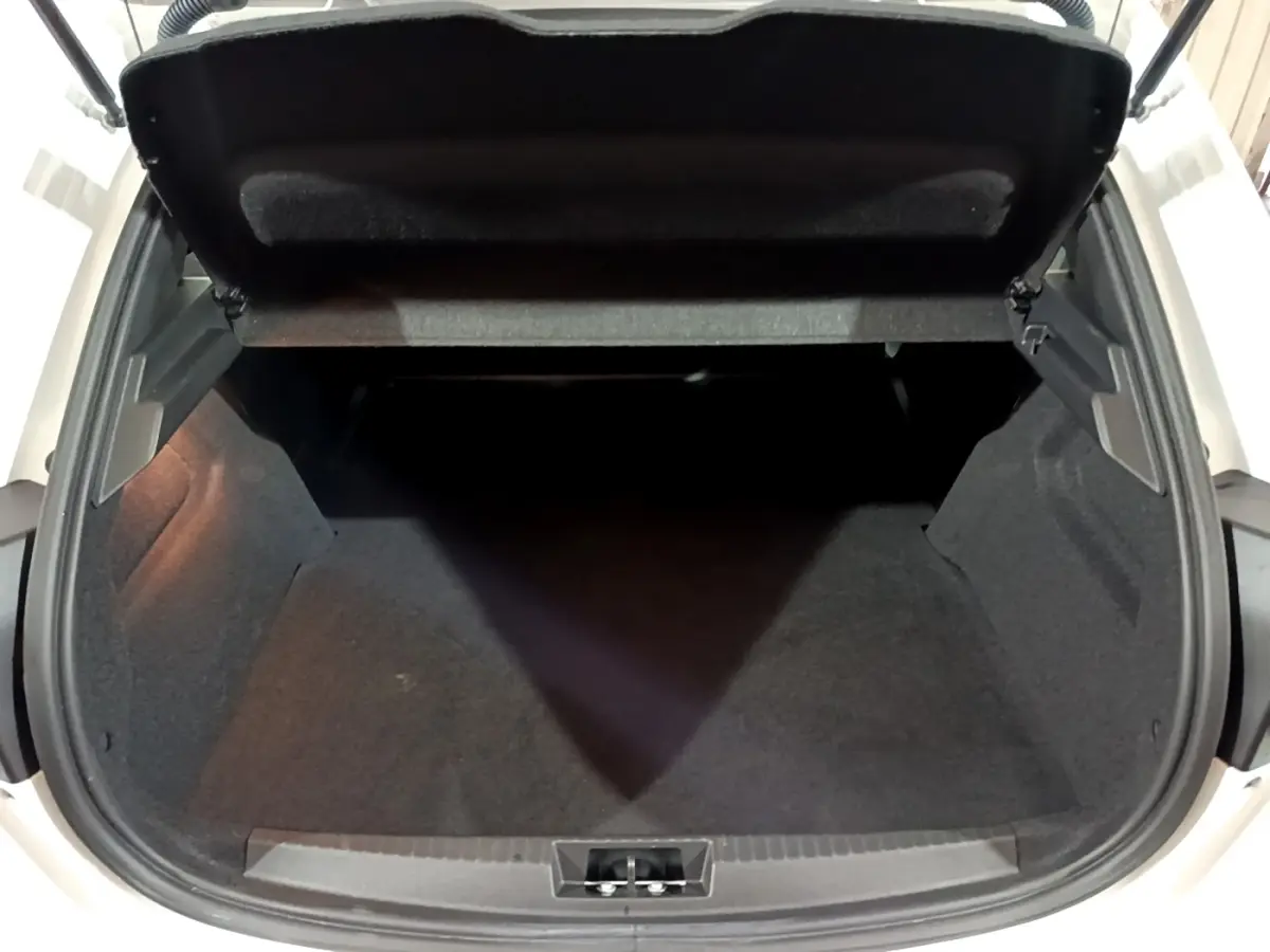 Vue plongeante sur le coffre ouvert d'une Peugeot 208 blanche, montrant l'espace de rangement vide et la doublure noire.