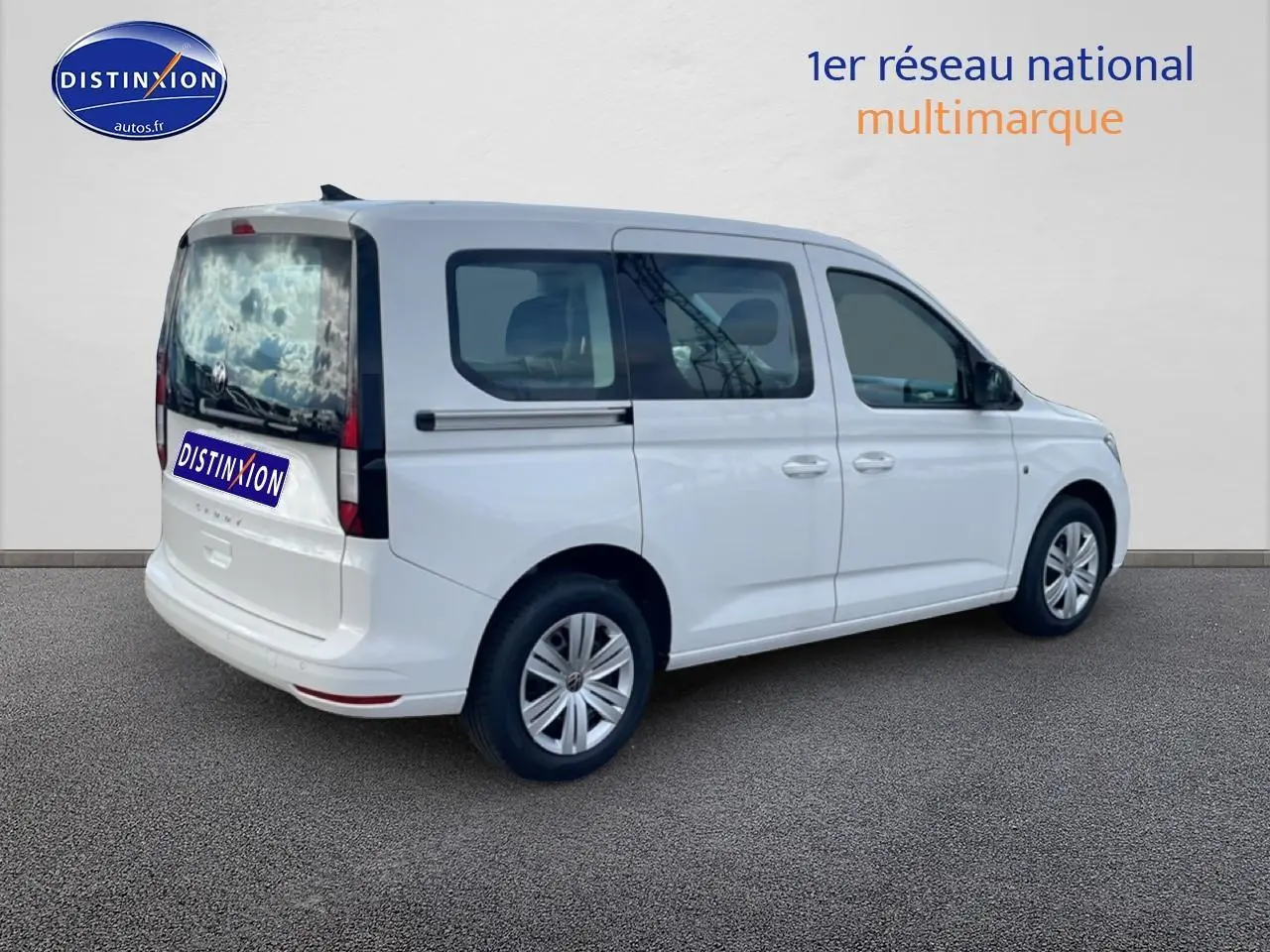 Volkswagen Caddy blanc vu en 3/4 arrière droit, avec vitres teintées et barres de toit noires.