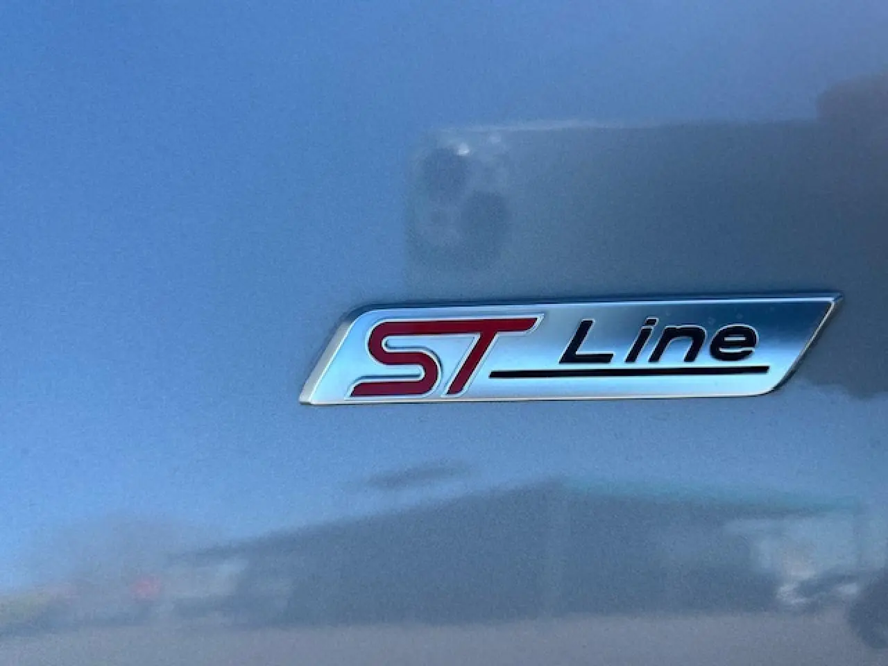 Gros plan sur le badge ST-Line rouge et noir sur la carrosserie gris magnetic d'un Ford Puma 2023.