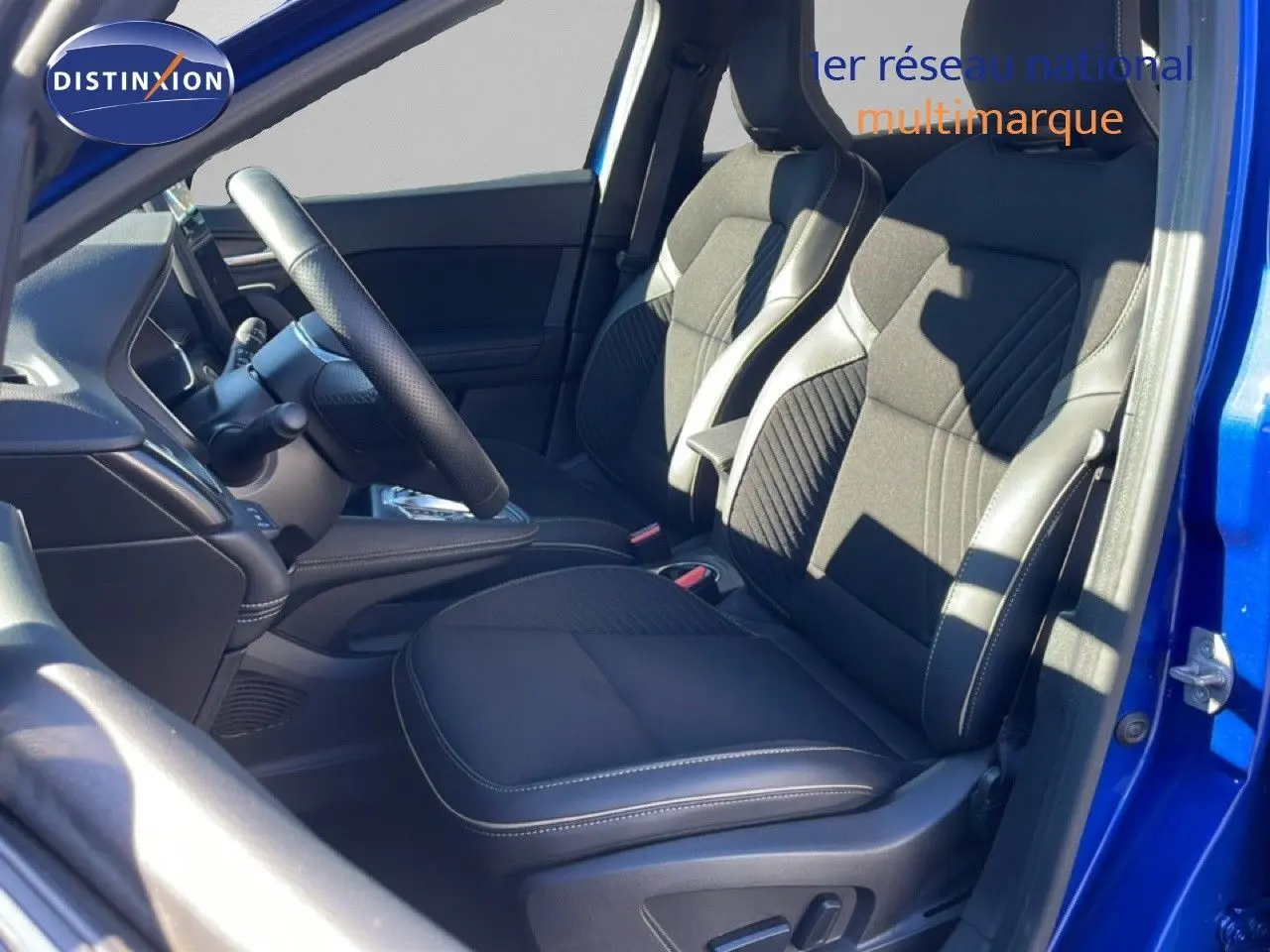 Vue intérieure côté conducteur du Renault Symbioz 2025 bleu iron metal, mettant en valeur les sièges tissu noir avec surpiqûres blanches.