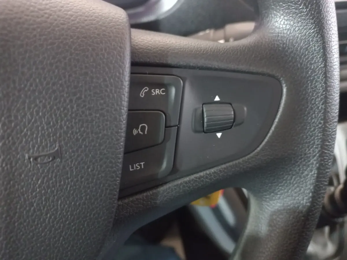 Gros plan sur les commandes noires du volant du Peugeot Traveller 1.5 BlueHDi gris clair, avec boutons SRC et LIST visibles.