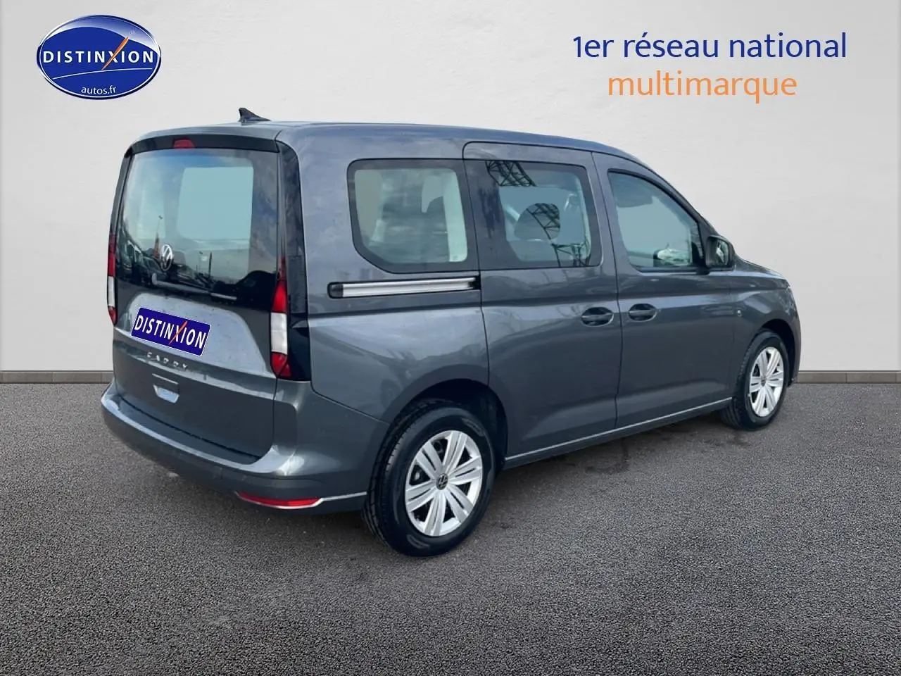 Vue 3/4 arrière droite d'un Volkswagen Caddy gris indien 2025 avec barres de toit et vitres teintées.