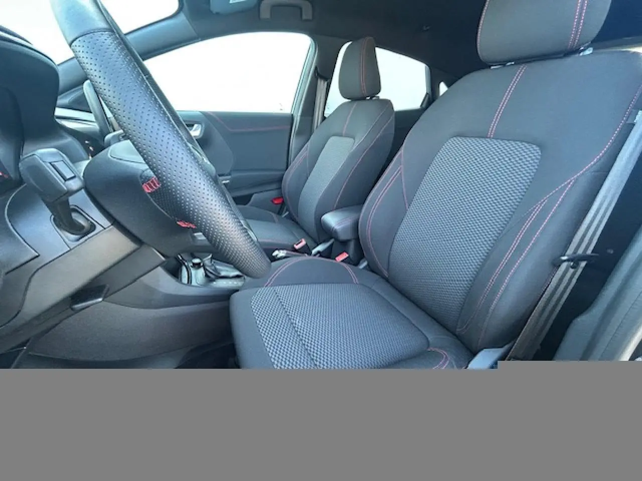 Intérieur avant du Ford Puma 2023, sièges noirs avec surpiqûres rouges et volant perforé ST-Line à méplat.