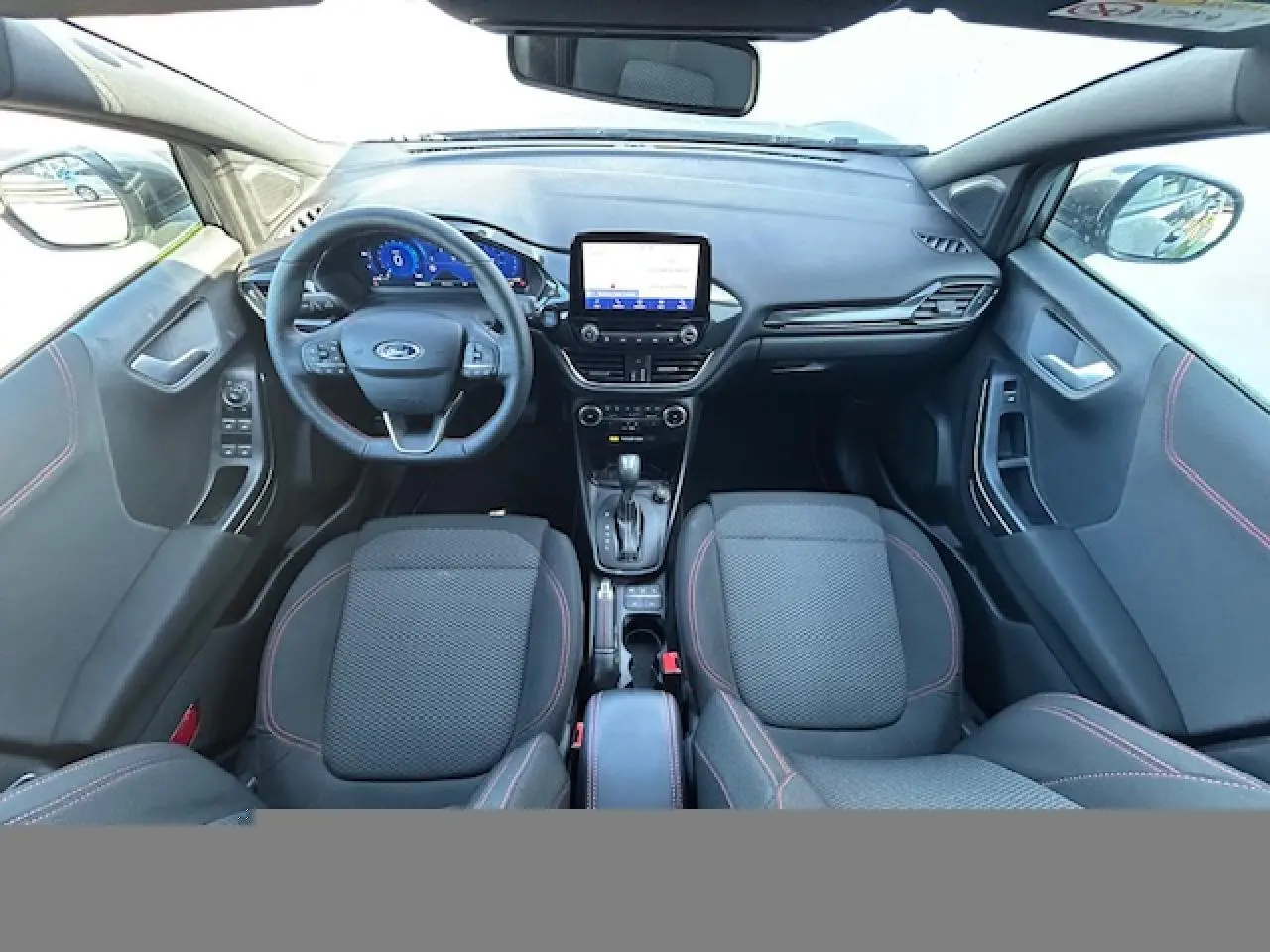 Vue intérieure avant du Ford Puma gris Magnetic 2023, volant ST-Line à méplat avec surpiqûres rouges et écran tactile central.