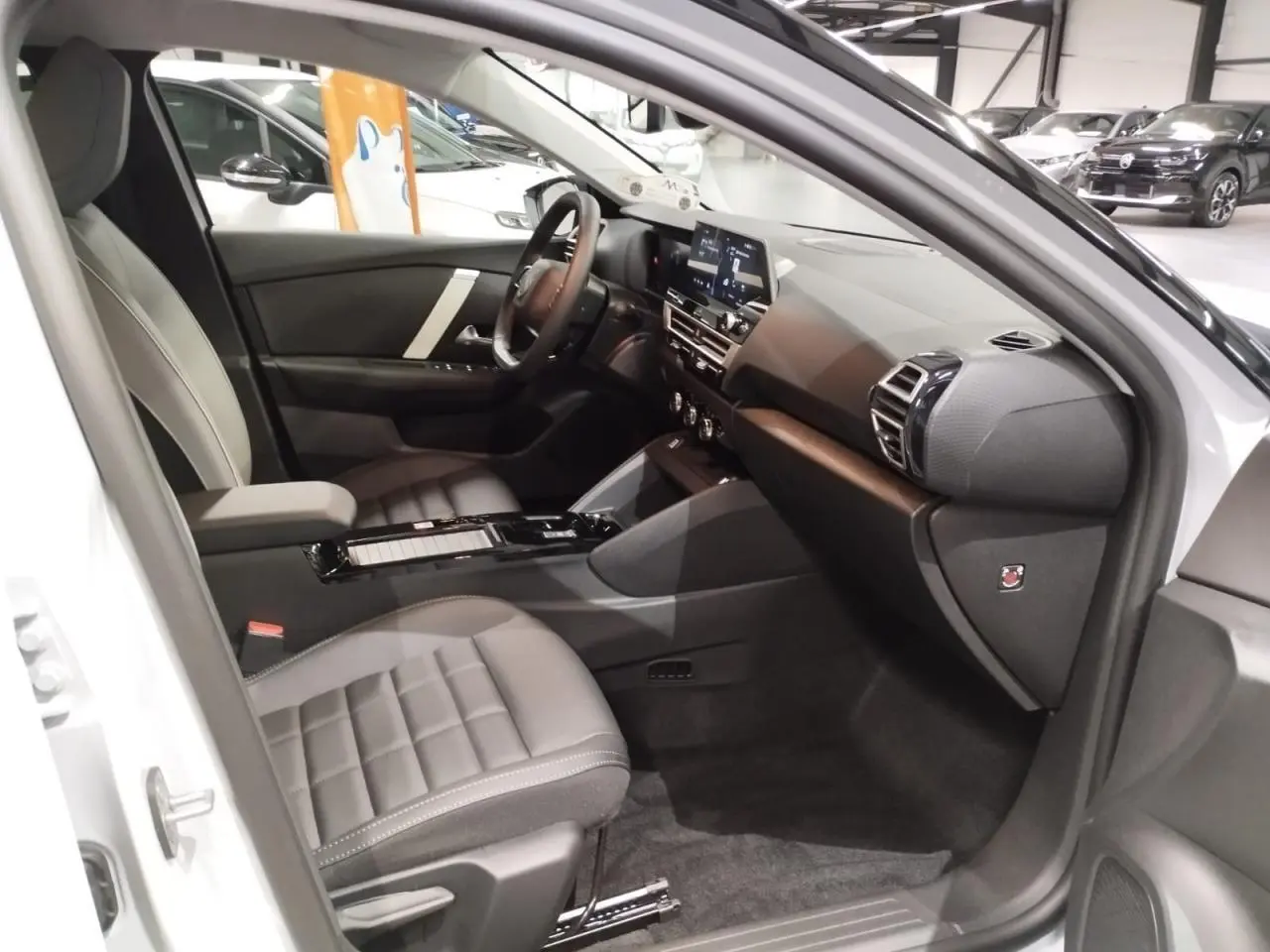 Vue intérieure côté passager avant de la Citroën C4 2025, sièges gris et tableau de bord noir moderne.