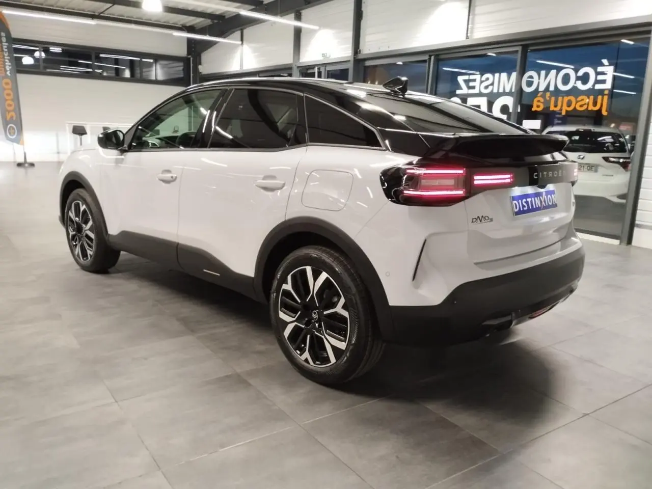 Vue 3/4 arrière droite d'une Citroën C4 blanche Okenite avec toit noir et jantes alliage 18'' dans un showroom.
