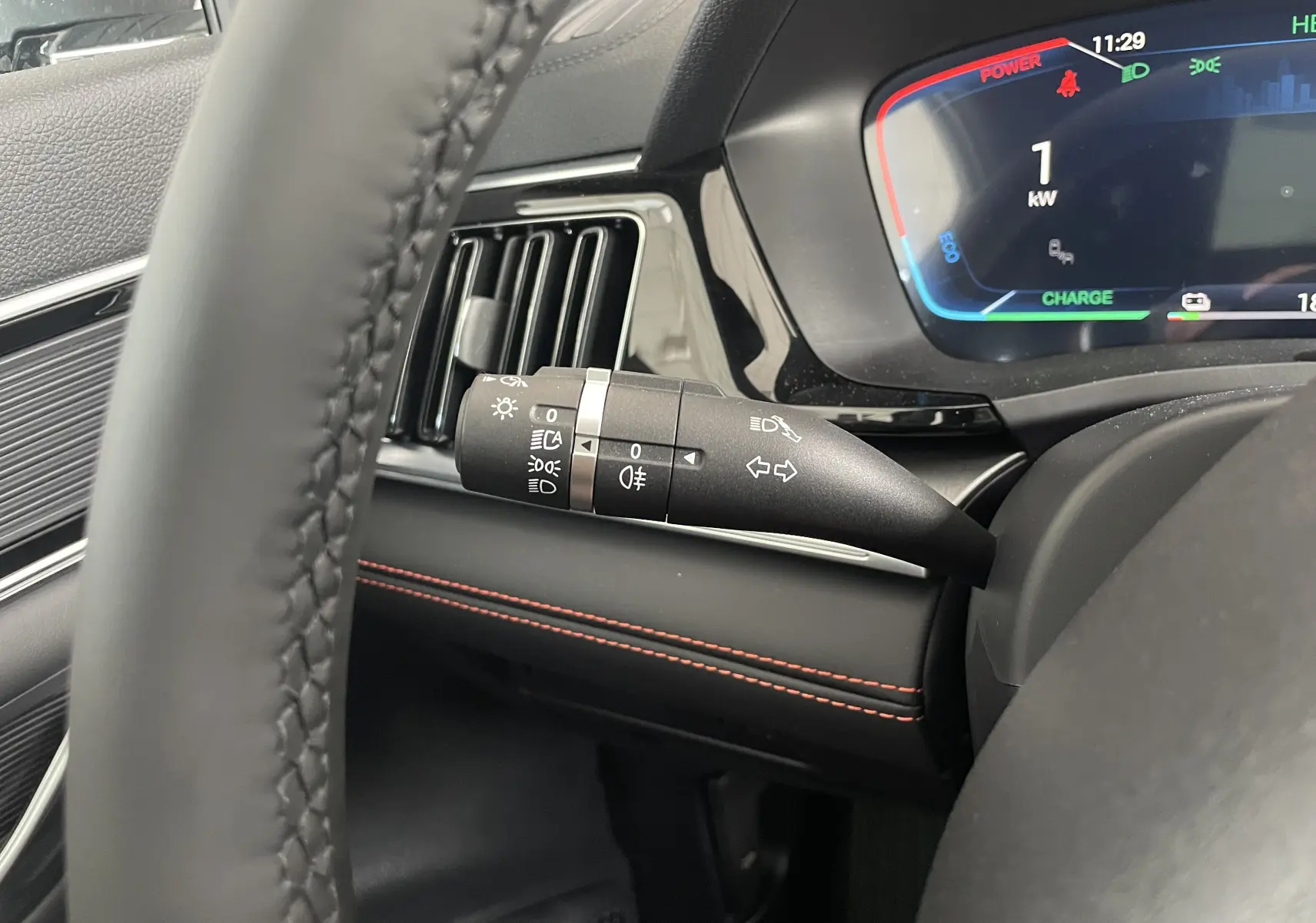 Gros plan sur la commande des phares et clignotants à gauche du volant dans l’habitacle noir avec surpiqûres rouges du BYD SEAL U 2025.