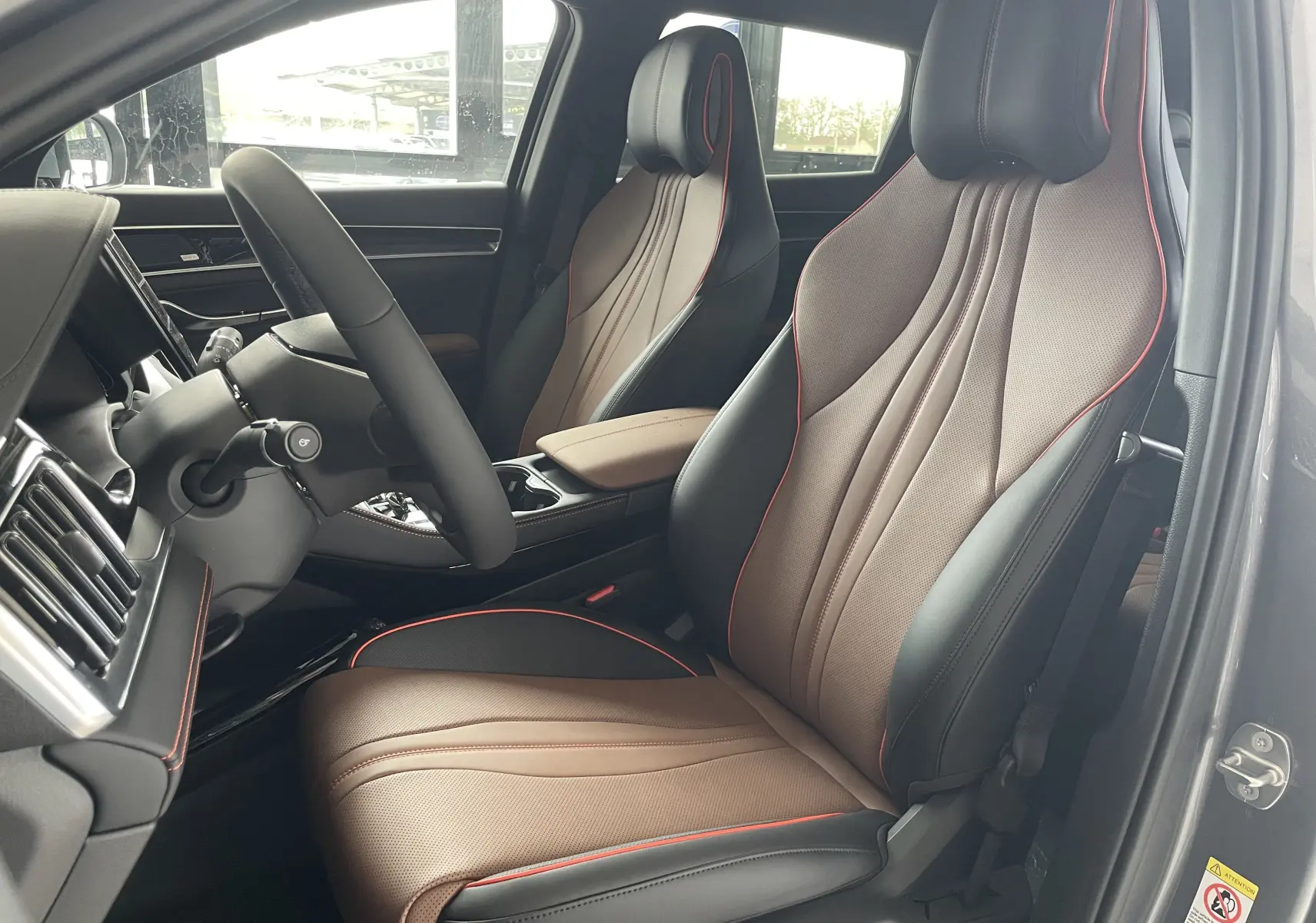 Vue intérieure côté conducteur du BYD SEAL U 2025, sièges en similicuir bicolore noir et marron avec surpiqûres rouges.