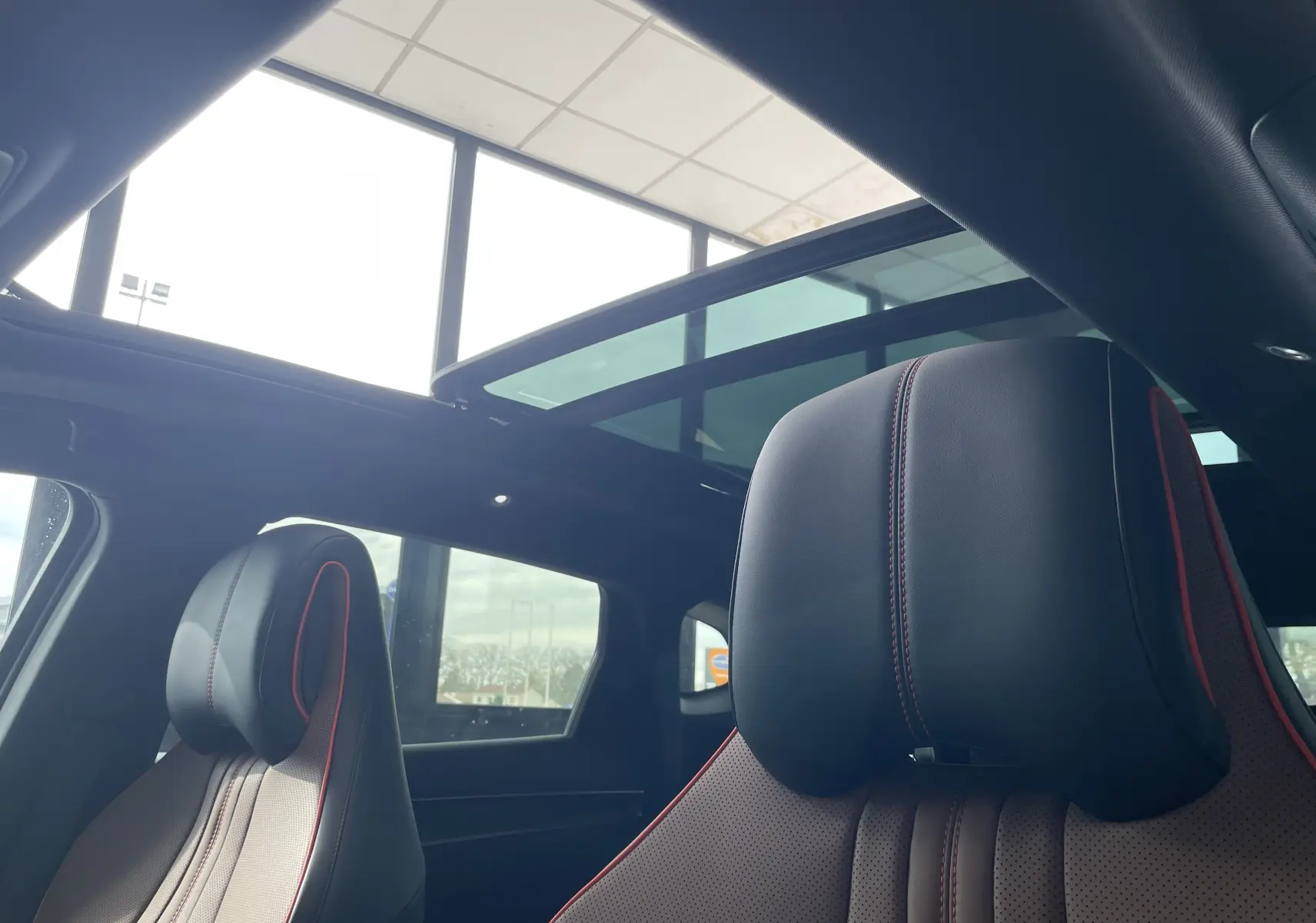 Vue intérieure sur les sièges avant noirs et marron avec surpiqûres rouges, sous un toit ouvrant panoramique vitré.