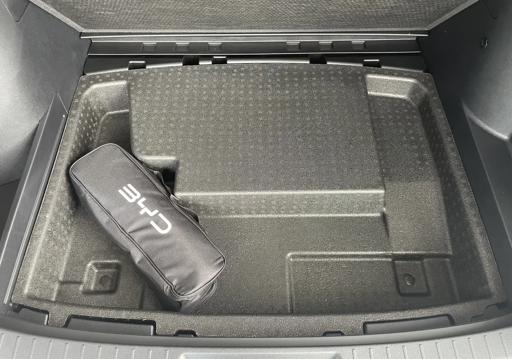 Vue plongeante sur le coffre du BYD SEAL U 2025 en TIME GREY, montrant un rangement avec sac de chargeur CHR noir.
