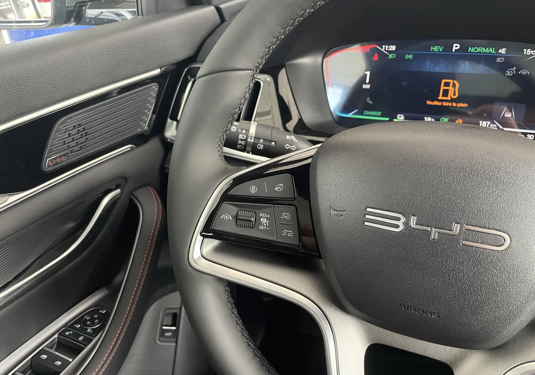 Gros plan sur le volant multifonction et le tableau de bord numérique du BYD SEAL U 2025, intérieur noir avec surpiqûres rouges.