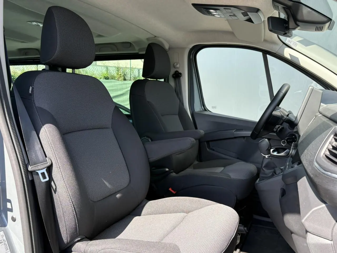 Vue intérieure côté conducteur du Renault Trafic Fourgon 2024, sièges confort gris foncé avec accoudoirs et volant visible.