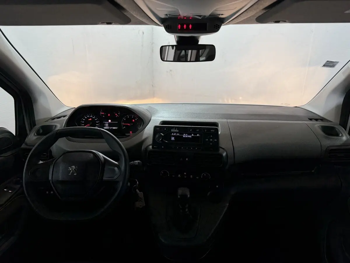 Vue intérieure frontale du tableau de bord et volant noir du Peugeot Rifter blanc, avec affichage digital et commandes centrales visibles.