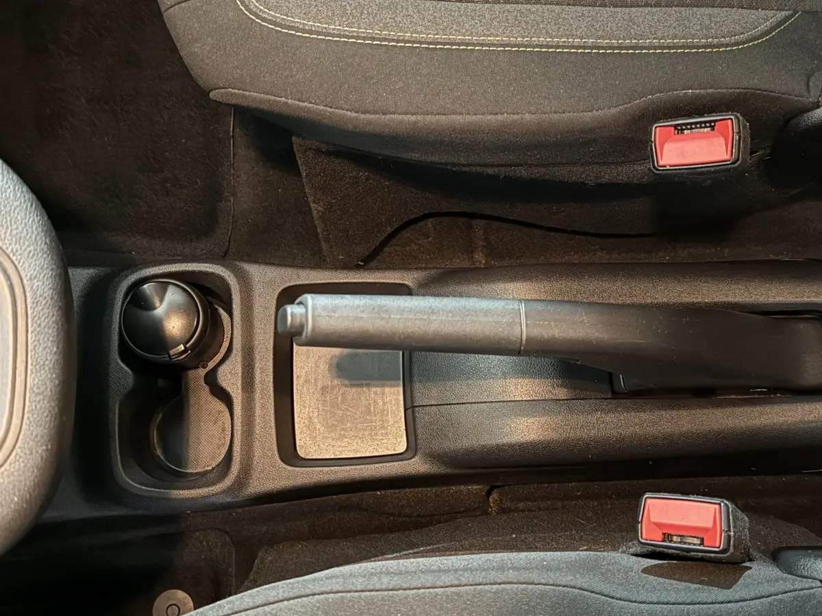 Vue rapprochée de la console centrale noire du Peugeot Rifter blanc, avec frein à main manuel et porte-gobelet.