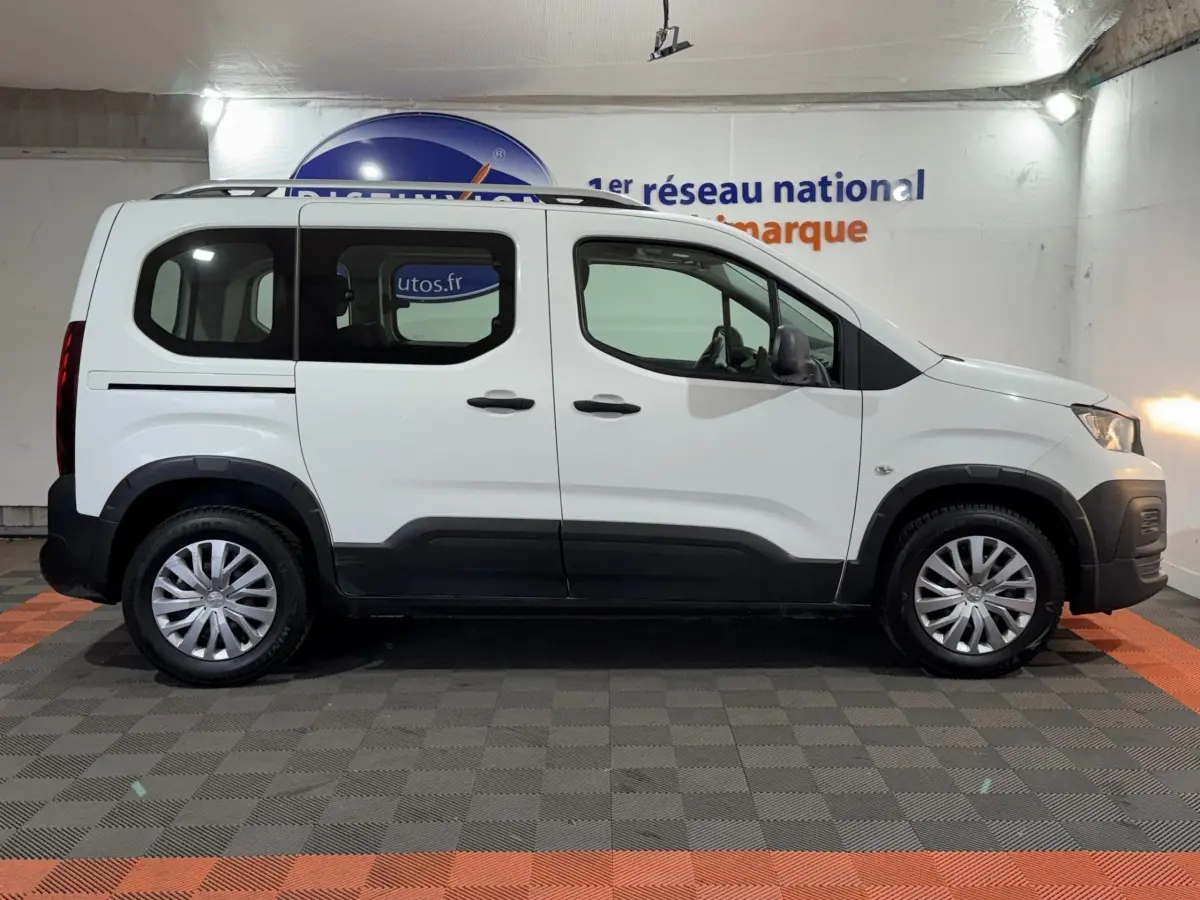 Vue de profil côté gauche d'un Peugeot Rifter blanc avec barres de toit chromées et jantes alliage.