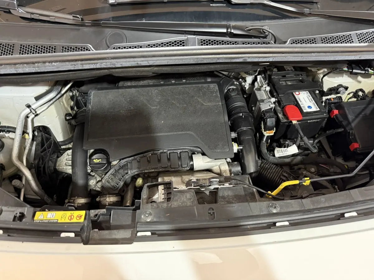 Vue plongeante sur le compartiment moteur d’un Peugeot Rifter blanc de 2019, montrant le moteur essence PureTech.