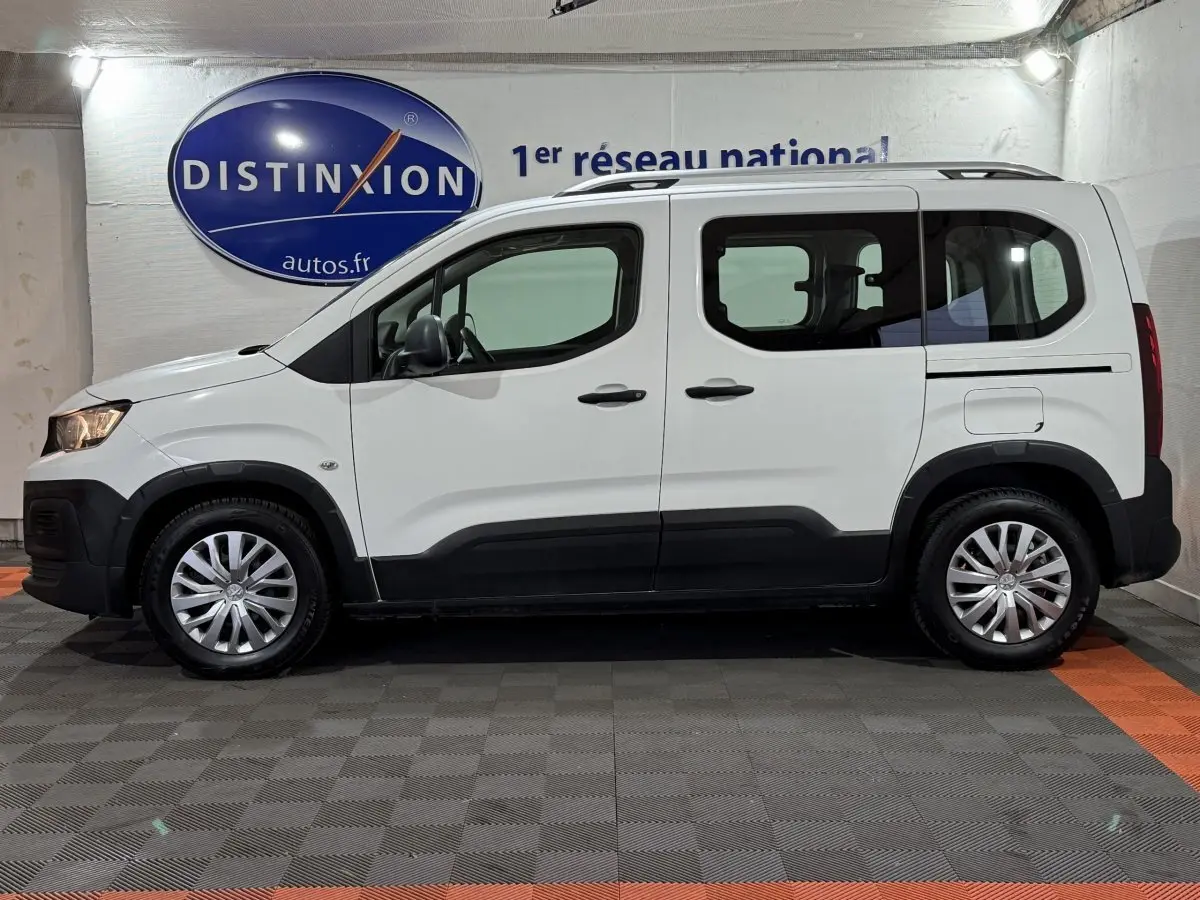 Vue de profil côté gauche d'un Peugeot Rifter blanc 2019 avec rails de toit chromés et jantes argentées.