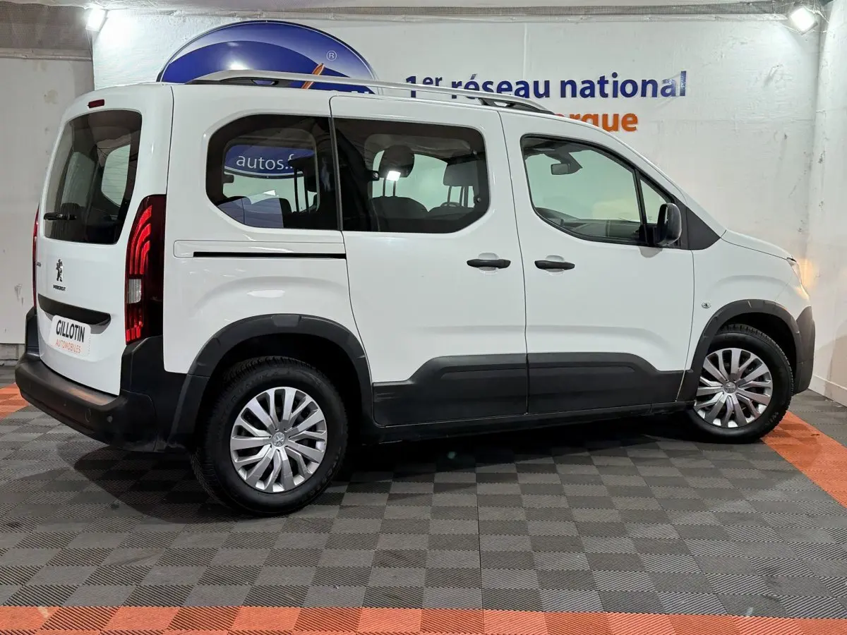 Vue latérale droite d'un Peugeot Rifter blanc 2019 avec rails de toit chromés et protections noires sur bas de caisse.