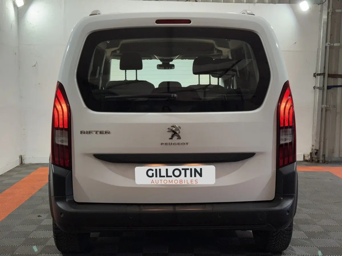 Vue arrière d’un Peugeot Rifter blanc de 2019 avec feux arrière allumés dans un garage.